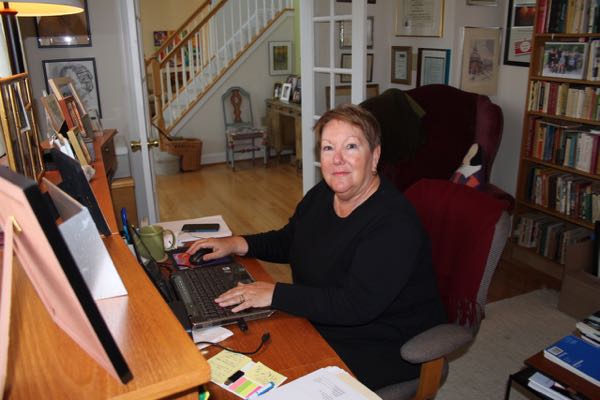 A photo taken by Katherine Cobb of me in my writing lair surrounded by the family photos, drawings and paintings that sustain me.